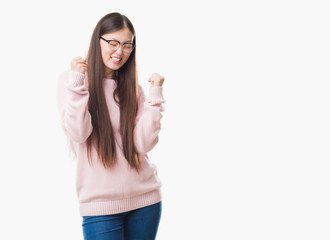 Young Chinese woman over isolated background wearing glasses very happy and excited doing winner gesture with arms raised, smiling and screaming for success. Celebration concept.