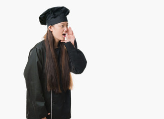 Young Chinese woman over isolated background wearing chef uniform shouting and screaming loud to side with hand on mouth. Communication concept.