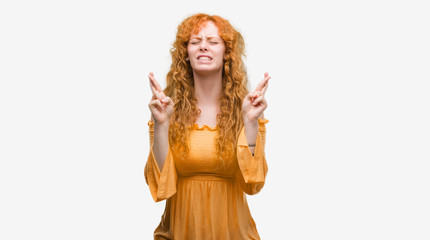 Young redhead woman smiling crossing fingers with hope and eyes closed. Luck and superstitious concept.