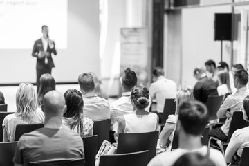 Speaker giving a talk in conference hall at business event. Focus on unrecognizable people in audience. Business and Entrepreneurship concept. Black and white image.