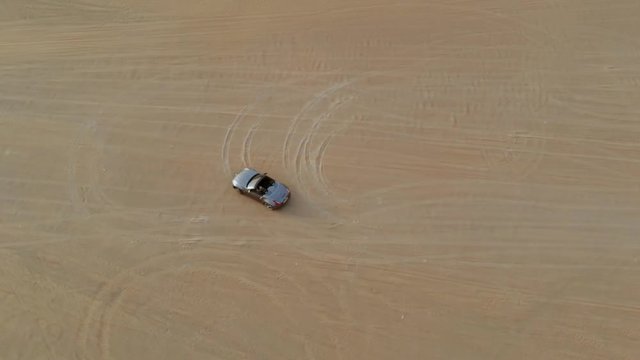 Grey convertible car filmed from distant above while making 8 circles in the sand.