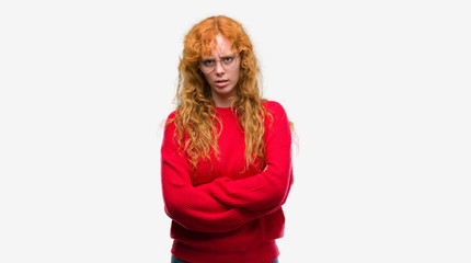 Young redhead woman wearing red sweater skeptic and nervous, disapproving expression on face with...