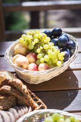 Closeup of basket with grapes, peaches and plumps on a wooden table, outdoor party or picnic