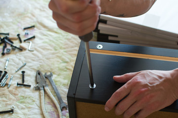 man holding a wooden box and fasten the screws and in the background are tools