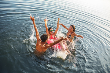 Young friends swimming and having fun in the lake.Female sitting on air mattress drinks lemonade ...