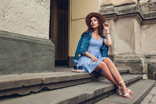 Outdoor portrait of young beautiful fashionable woman wearing stylish accessories. Girl sitting on stairs in city
