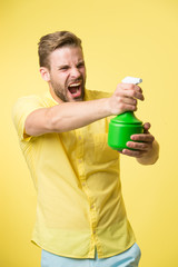 Macho hold plastic spray bottle as gun yellow background. Guy with water spray in hand pretend...