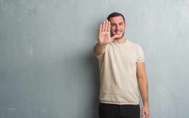 Young caucasian man over grey grunge wall doing stop sing with palm of the hand. Warning expression...