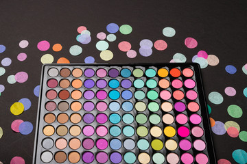 Closeup of makeup eyeshadow palette with confetti on black