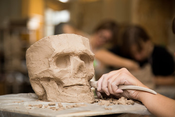 Sculptor modeling a skull out of raw clay with hands in a sculpting studio workshop