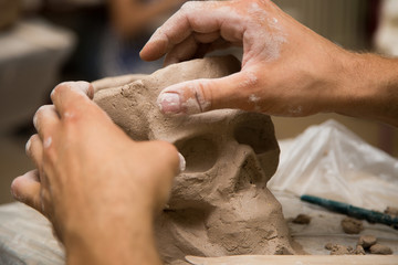 Sculptor modeling a skull out of raw clay with hands in a sculpting studio workshop