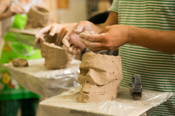 Sculptor modeling a skull out of raw clay with hands in a sculpting studio workshop