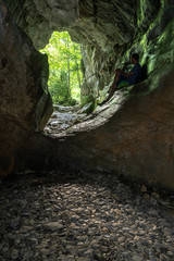 Hombre sentado dentro de una impresionante cueva de paredes verdes mirando hacia el exterior. Cueva del Ibón, Valle de Roncal, España. 