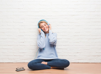 Beautiful young woman sitting on the floor listening music wearing headphones at home with a happy face standing and smiling with a confident smile showing teeth