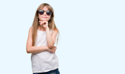 Young blonde toddler wearing sunglasses serious face thinking about question, very confused idea