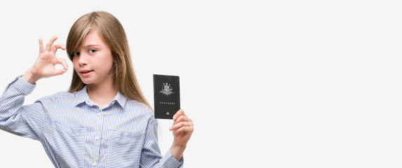 Young blonde toddler holding australian passport doing ok sign with fingers, excellent symbol