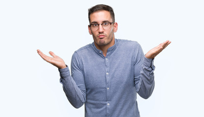Fototapeta premium Handsome young elegant man wearing glasses clueless and confused expression with arms and hands raised. Doubt concept.