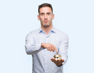 Handsome young man holding hotel ring bell with a confident expression on smart face thinking serious