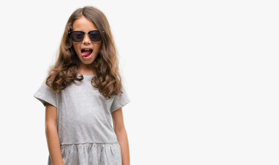 Brunette hispanic girl wearing sunglasses sticking tongue out happy with funny expression. Emotion concept.