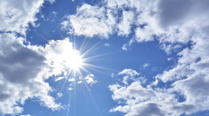 The sun shines among the white cumulonimbus clouds on the blue sky