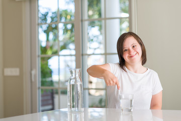 Down syndrome woman at home drinking water very happy pointing with hand and finger