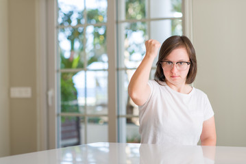 Down syndrome woman at home annoyed and frustrated shouting with anger, crazy and yelling with raised hand, anger concept