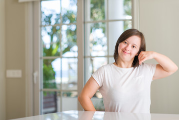 Down syndrome woman at home smiling doing phone gesture with hand and fingers like talking on the telephone. Communicating concepts.