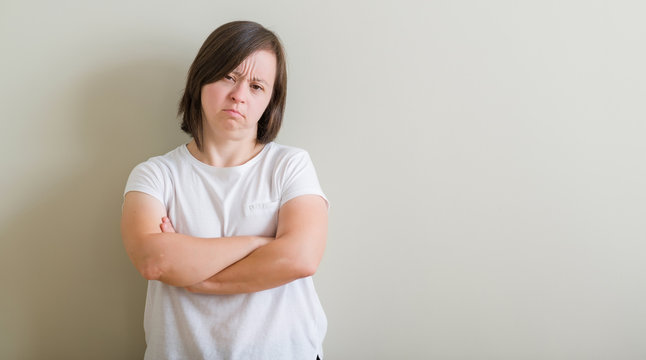 Down syndrome woman standing over wall skeptic and nervous, disapproving expression on face with crossed arms. Negative person.