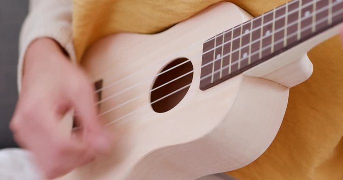 Woman play ukulele and sitting on sofa at home