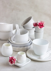 Fototapeta na wymiar Set of different white ceramic dishes on a light grey background. Elegant white tableware. Minimalistic still life. Soft light, high key. 