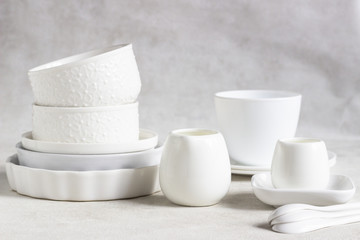 Set of different white ceramic dishes on a light grey background. Elegant white tableware....