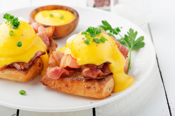 Eggs benedict with bacon on white  wooden background . 
