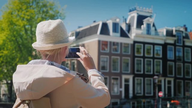 A middle-aged woman takes pictures of beautiful buildings and a canal in Amsterdam. Travel Europe concept