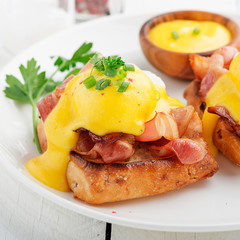 Eggs benedict with bacon on white  wooden background . 