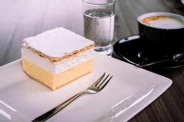 Delicious desset cream cake on the white square plate served with cappucino and water at Bled lake, Slovenia