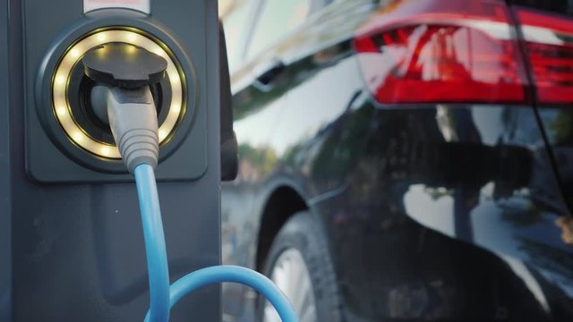 An electric car is charging on a city street, a close-up of a cable connected to a car