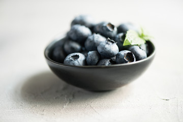 Blueberries, summer season, berries in black bowl. Selective focus, toned image, closeup.