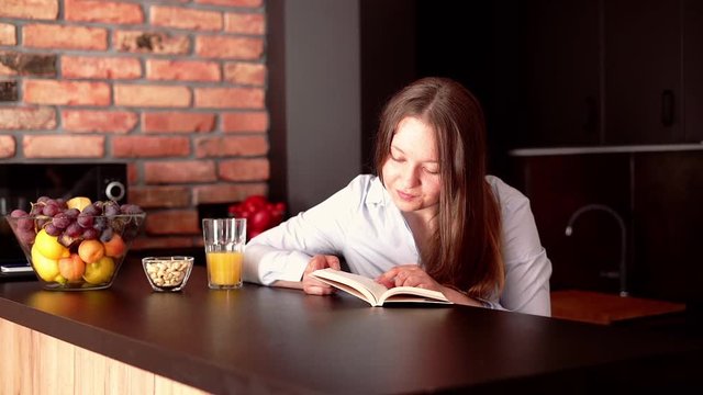 Young, happy woman reading book by table at home
