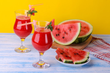 Watermelon smoothies next to a fresh ripe watermelon on a blue wooden table and on a yellow background