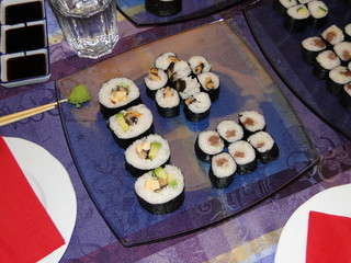 Cena de rollos de sushi maki casera. Presentación de platos variados de comida japonesa en comedor de casa. Receta con ingredientes asiáticos con pescado crudo, alga nori y arroz.