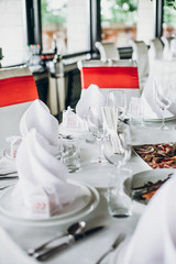 elegant wedding table with food, silver cutlery, empty glasses. settings with red decoration and white silk chairs and napkins. luxury catering in restaurant for wedding reception