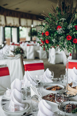 stylish wedding table setting. elegant wedding table with red roses decoration and white silk chairs and napkins. luxury catering in restaurant for wedding reception