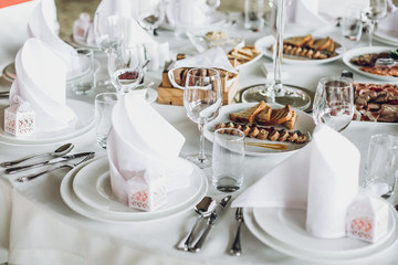 luxury catering in restaurant for wedding reception. elegant wedding table with food, silver cutlery, empty glasses, white silk chairs and napkins. stylish wedding table setting