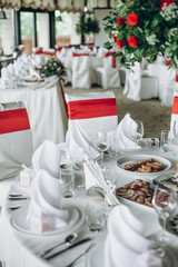 stylish wedding table setting. elegant wedding table with red roses decoration and white silk chairs and napkins. luxury catering in restaurant for wedding reception