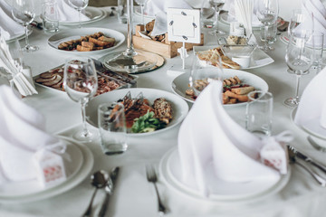 luxury catering in restaurant for wedding reception. elegant wedding table with food, silver cutlery, empty glasses, white silk chairs and napkins. stylish wedding table setting