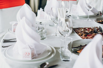 elegant wedding table with food, silver cutlery, empty glasses. settings with red decoration and white silk chairs and napkins. luxury catering in restaurant for wedding reception