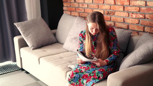 Young, cute woman reading newspaper on sofa at home
