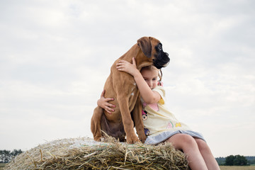 Young dog with little girl sitting  on top of haystack.