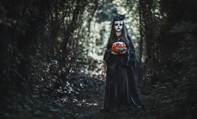 Happy Halloween! horrible creepy child girl in  witch costume with pumpkin in forest