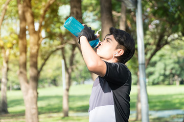 Attractive man drinking water from bottle after worker in the park. Men raising bottles drink water to refresh after exercise at outdoor.
